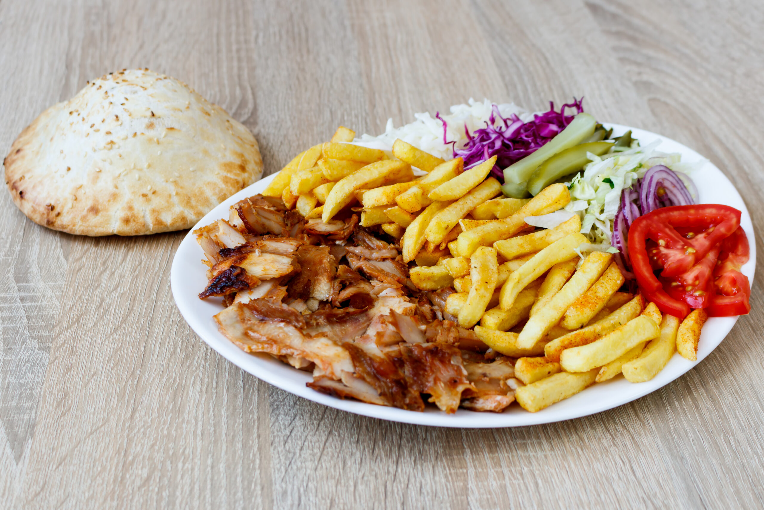 Chiken Doner Kebab on the plate with bread, french fries, tomatoes, onion, pickles and salad on a wooden background. Grilled chicken meat with vegetables.